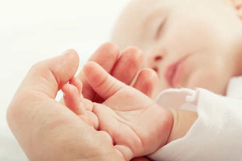 Śpiące niemowlę położyło rączkę na dłoni mamy