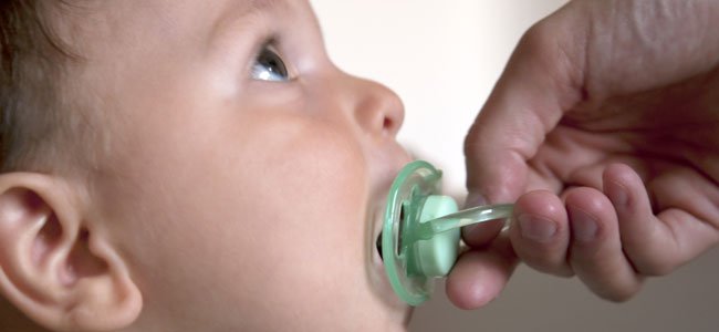 Dziecko ssące smoczek trzymany w ręku przez rodzica - nadmierne używanie smoczka