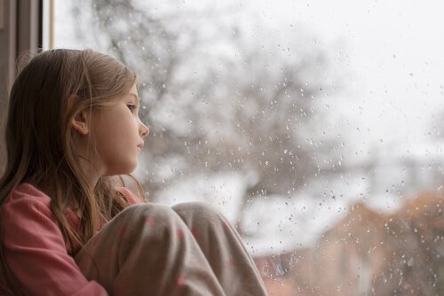 Dziewczynka patrząca smutno przez okno, przeżywająca zły nastrój rodziców