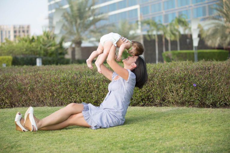 Mama siedząca na trawie podnosząca niemowlę - jak świętować pierwsze urodziny Twojego dziecka