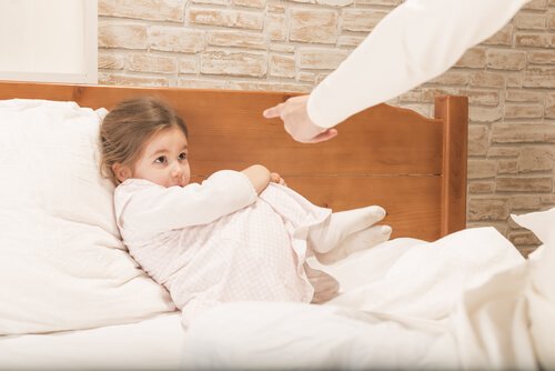 Ręka grożąca palcem dziewczynce leżącej na łóżku