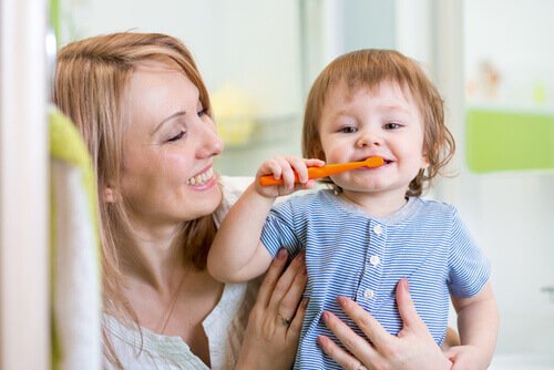 Uśmiechnięta mama przytulająca dziecko samodzielnie myjące zęby