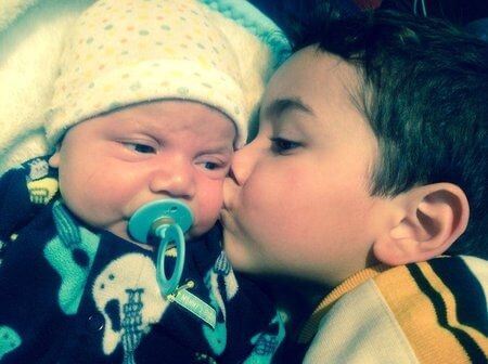 Chłopiec całujący niemowlę w policzek - zazdrość o młodsze rodzeństwo