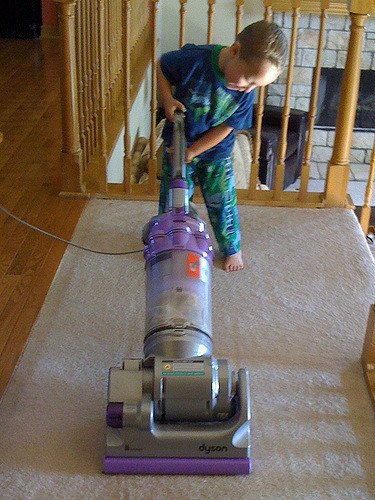 Chłopiec odkurzający dywan, wykonujący obowiązki domowe