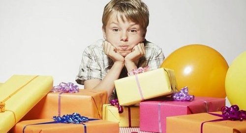 Chłopiec opierający brodę na dłoniach siedzący między prezentami