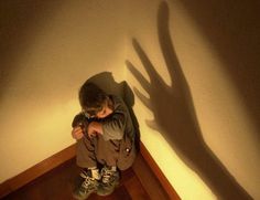 Chłopiec skulony w rogu, chowający się przed cieniem ręki na ścianie