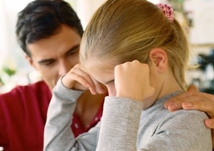 Dziewczynka z głową podpartą na rękach i gładzący ją po plecach tata