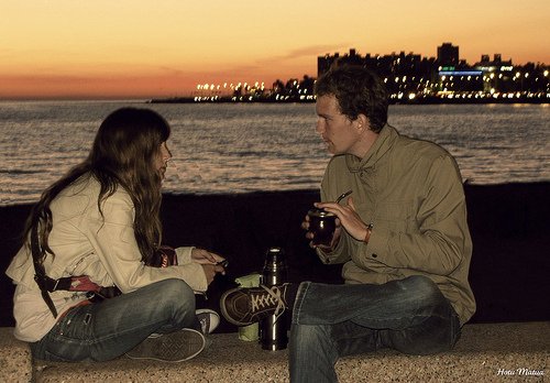 Kobieta i mężczyzna siedzący na murku o zachodzie słońca i pijący piwo
