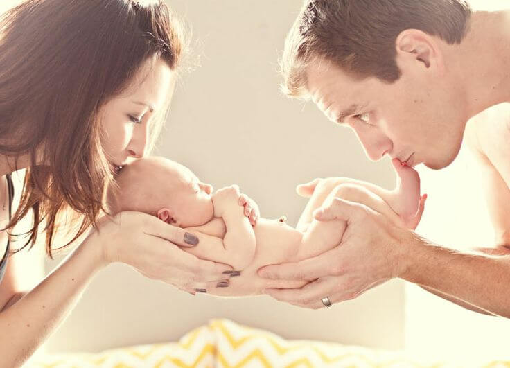 Mama i tata całujący niemowlę w nóżki i główkę - miłość mamy