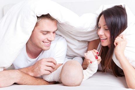 Rodzicielstwo - mama i tata z kołdrą na głowach bawiący się z dzieckiem