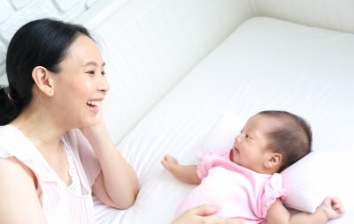 Mama uśmiechająca się do niemowlęcia leżącego na łóżku