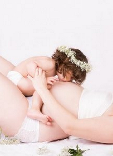 Mama w ciąży trzyma dziecko, które całuje jej brzuch