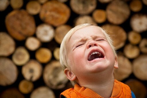 Płaczący chłopiec na tle drewnianej ściany