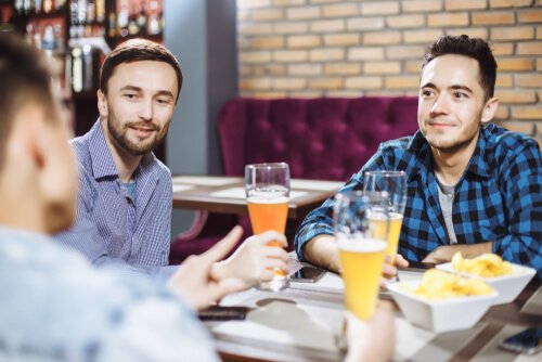 Trzech mężczyzn siedzących przy stoliku w barze i pijących piwo