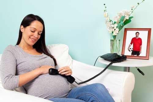 Uśmiechnięta mama trzyma telefon przy brzuchu, aby dziecko było szczęśliwe przed narodzinami