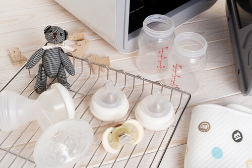 Butelki i smoczki leżące na suszarce z pluszowym misiem
