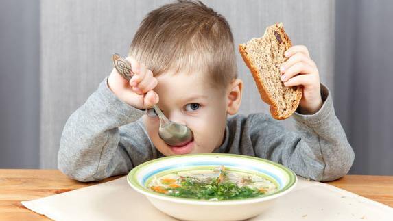 Chłopiec jedzący zupę trzymający w dłoni kawałek chleba