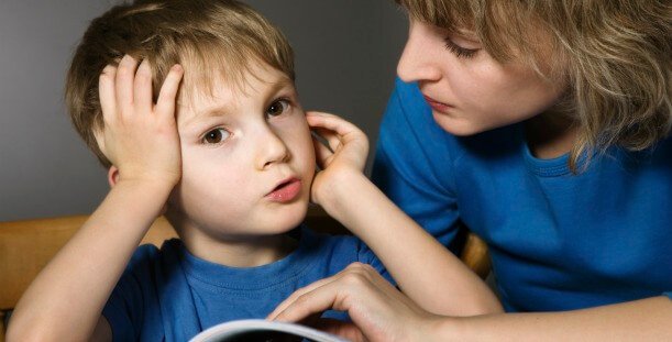 Chłopiec opierający twarz na ręku i pochylająca się nad nim mama pokazująca cierpliwość