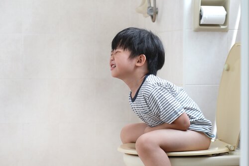 Chłopiec siedzący na toalecie, trzymający się za brzuch