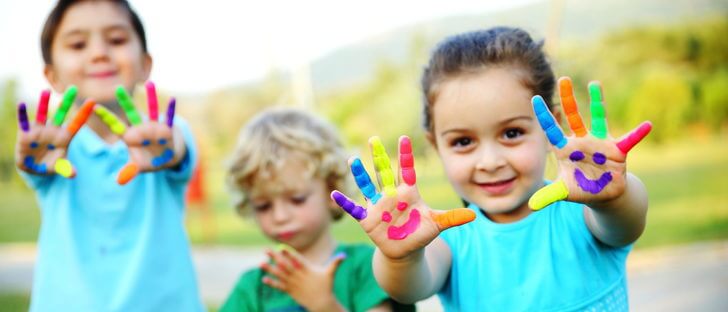 Dwie dziewczynki i chłopiec wyciągający przed siebie ręce z kolorowymi palcami