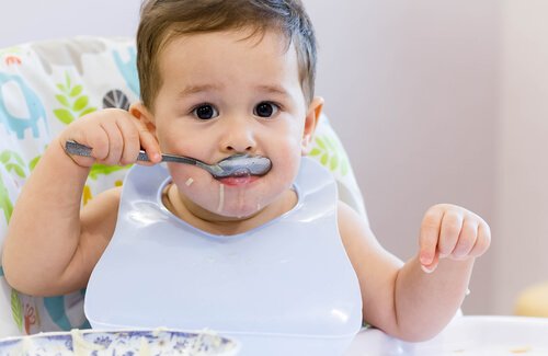 Dziecko w śliniaku z zalaną brodą, jedzące łyżką zupę - nauka samodzielnego jedzenia