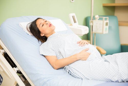Głęboko oddychająca kobieta w ciąży leżąca na łóżku szpitalnym - znieczulenie zewnątrzoponowe podczas porodu