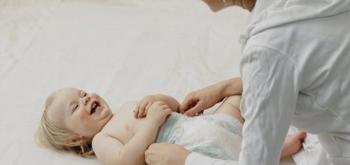 Jak łaskotać i całować dziecko po brzuchu - mama bawi się z roześmianym niemowlęciem