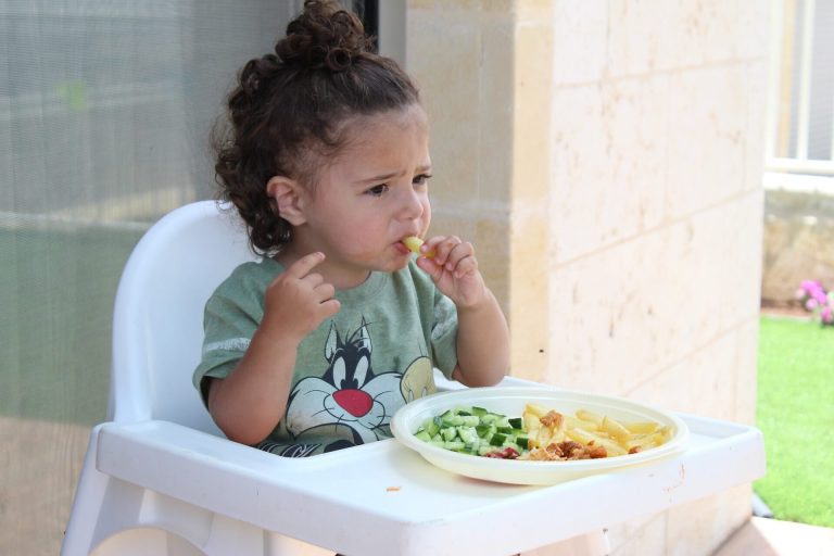Jedząca dziewczynka siedząca na krześle do karmienia, próbująca najlepsze pokarmy dla dziecka