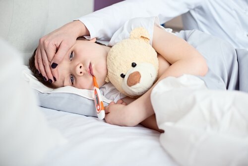 Leżący na boku chłopiec z termometrem w ustach i mama przykładająca mu rękę do czoła
