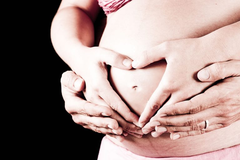 Mama i tata obejmujący brzuch w ciąży, układający dłonie w kształt serca