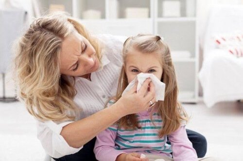 Mama pomagająca córce dmuchać nos w chusteczkę