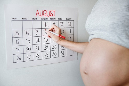Mama w ciąży skreślająca dni w kalendarzu ściennym - wyliczanie daty porodu