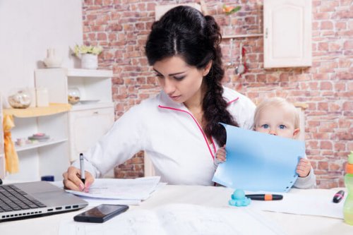 Mama przy stole z córką na kolanach, pisząca pracę - macierzyństwo i studiowanie