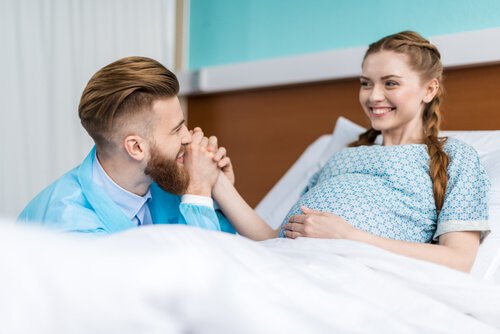 Mężczyzna trzymający kobietę w ciąży leżącą w łóżku za dłoń