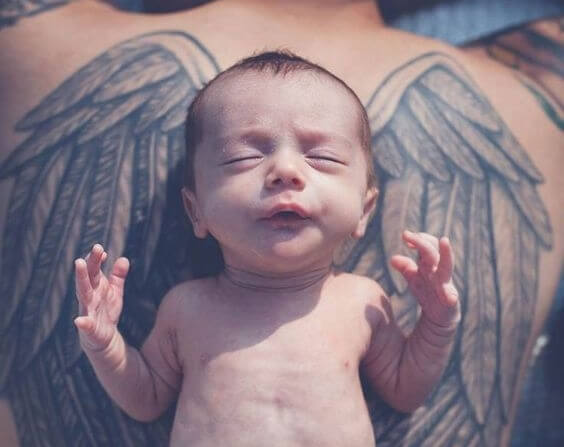Niemowlę leżące na plecach taty z tatuażem skrzydeł