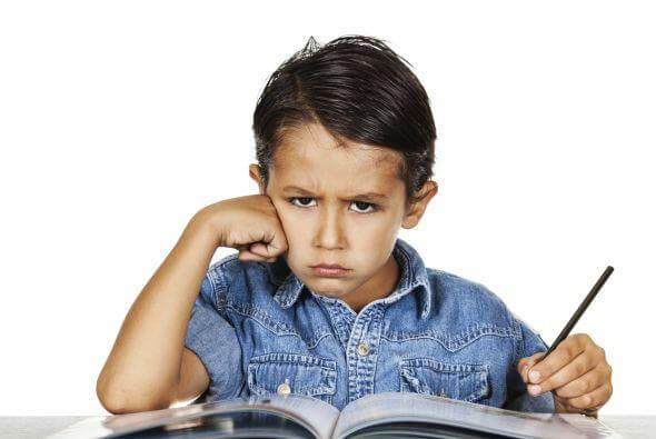 Obrażony chłopiec siedzący z ołówkiem w ręku nad książką