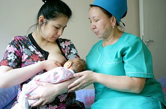Położna podtrzymująca dziecko przy piersi karmiącej mamy