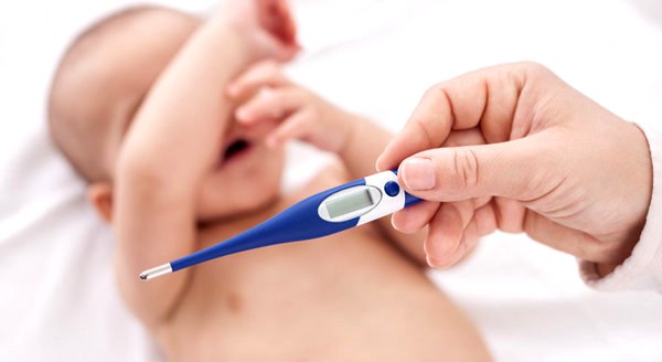 Ręka trzymająca elektroniczny termometr, w tle płaczące niemowlę