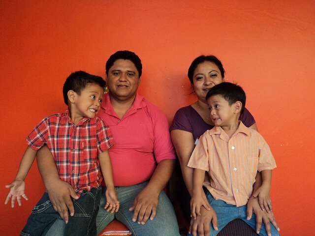 Siedzący obok siebie mama i tata, każdy trzyma na kolanach syna