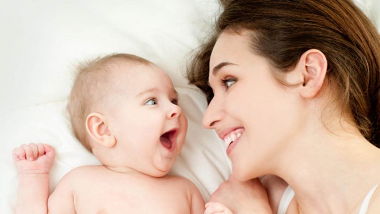 Śmiejący się mama i niemowlę leżący na białej pościeli