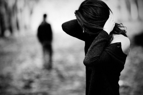 Smutna kobieta z twarzą zakrytą włosami, w tle sylwetka odchodzącego mężczyzny - cierpienie emocjonalne po odejściu rodzica