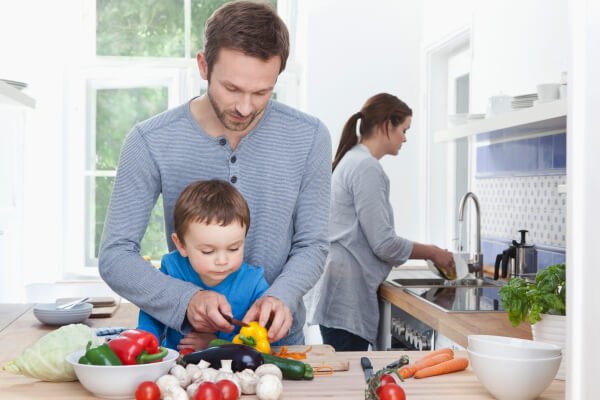 Tata krojący z dzieckiem warzywa w kuchni i mama w tle - pamiętaj, że nie jesteś służącą dziecka