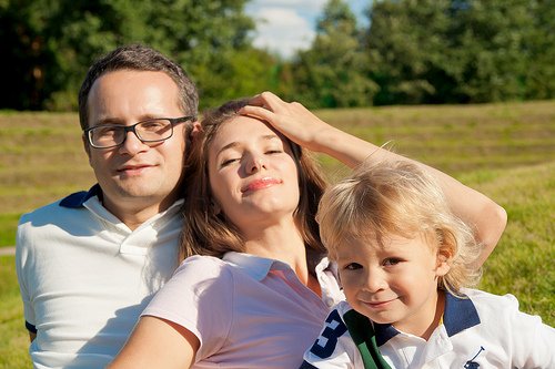 Uśmiechnięci tata, mama i syn robiący sobie selfie na tle łąki