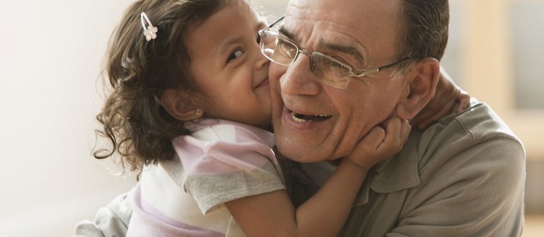 Uśmiechnięta dziewczynka przytulająca się do dziadka i całująca go w policzek - dawanie całusów przez dziecko