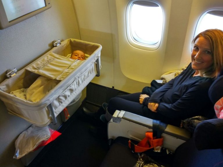 Uśmiechnięta mama w samolocie z dzieckiem śpiącym w kołysce - podróżowanie z niemowlęciem