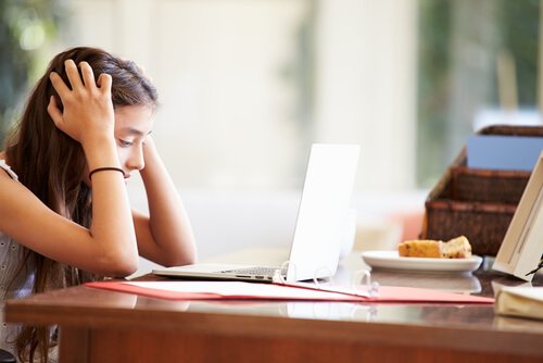 Dziecko ma problemy w szkole - dziewczynka siedzi przy biurku i trzyma się za głowę