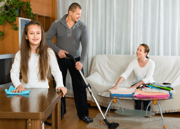 Dziewczynka wycierająca stół, tata odkurzający dywan i mama składająca pranie