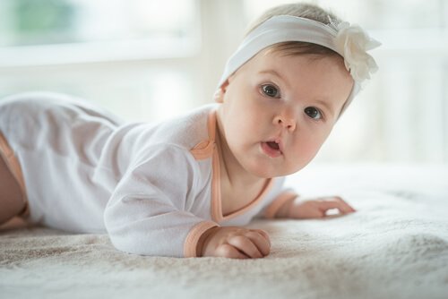 Dziewczynka z opaską na głowie raczkująca po dywanie - szósty miesiąc życia dziecka to początek raczkowania