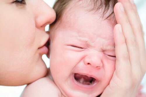 Mama całująca płaczące niemowlę w głowę - dziecko płacze, gdy jest mu źle