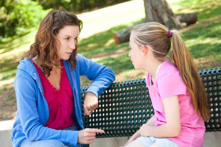 Mama i córka siedzące na ławce w parku i rozmawiające ze sobą